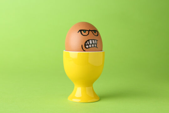 Egg with drawn angry face in cup on green background