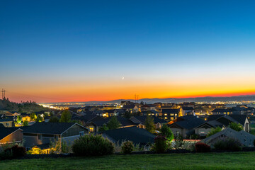 A crescent moon moves across the red late summer sunset sky over the lights of the cities of...