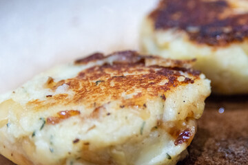 A single uncooked round salt cod fishcake prepared for frying. The mixture of savory, potato, salt codfish, and butter is shaped into a small patty as a dish once fried in butter and browned goldenly.