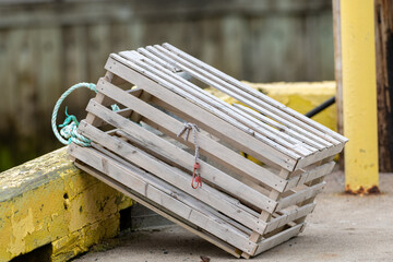 A single wooden lobster trap on the side of an industrial wharf. The lobster pot hangs over the...