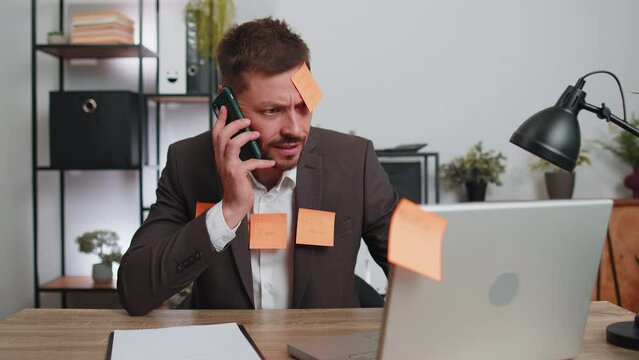 Tired exhausted businessman in suit working on laptop at office with many sticker task inscriptions. Freelancer man busy occupation feels sad boredom overworked multitasking. Panic attack, deadline