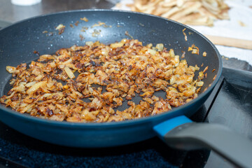 A large black colored iron frying pan full of sweet white onions minced and chopped into being fried or sauteed in butter. The edges of the diced onion have browned and caramelized to sweeten. 