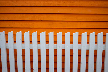 Exterior horizontal clapboard wooden bright orange wall with the sun shining on it. There's a white...