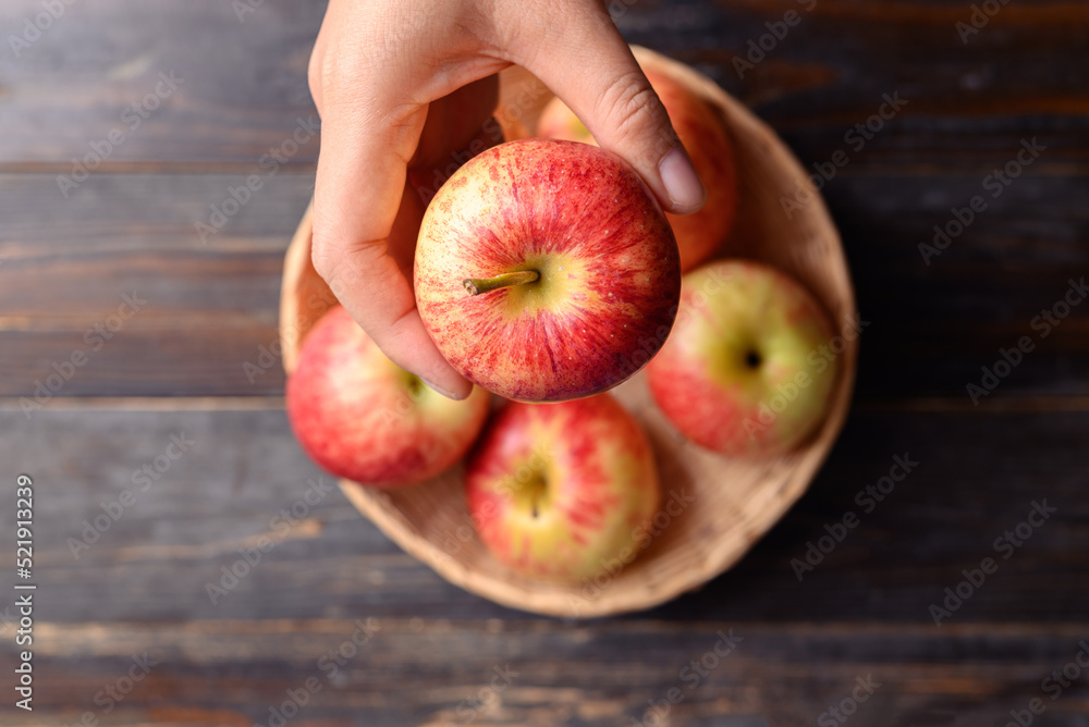 Wall mural Red apple fruit in basket with hand on wooden background, Table top view