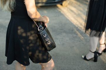 Girl with black bag in black dress on street. Girls in parking lot. Clothing details.