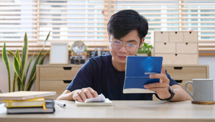 Asian man using laptop computer and counting taxes or house expenditures.