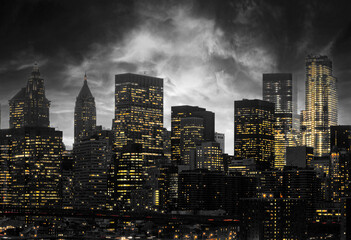 Yellow lights shining from the buildings of a black and white New York City skyline at night with dark clouds swirling