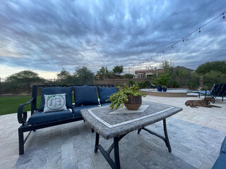A travertine tiled pool deck with a spa and outdoor kitchen on a desert landscaped backyard in Arizona.