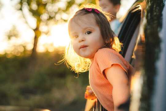 Portrait of a baby girl sticking her head out the car window to admire nature. Summer vacation fun. Happy family, childhood.