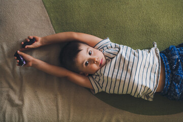 Top view of a boy lying on his back on the bed looking sleepily into the camera. Expression on his...