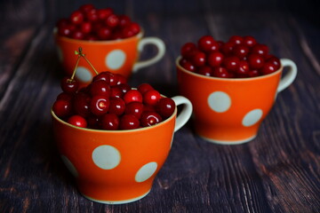 Three cups with red ripe juicy fresh sweet cherries harvest close up on dark wooden boards. Selective focus