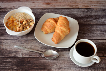 A plate of oatmeal with nuts, raisins, two fresh croissants and a cup of coffee.