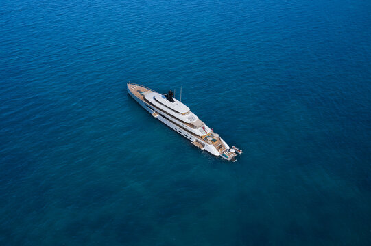 Modern big white yacht on the water top view. White big yacht at anchor aerial view. Mega yacht on water aerial view.