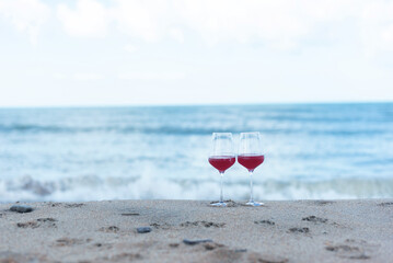 Fototapeta na wymiar Two glasses of red wine stand on the shore of the blue sea