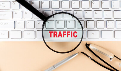 Text TRAFFIC on keyboard with magnifier , glasses and pen on beige background