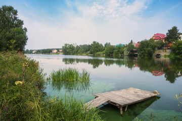 Summer day in the village on a pond with wooden footbridges for swimming and fishing. Russia, Ural