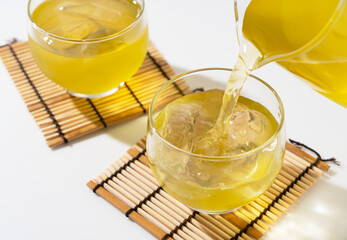 Pouring green tea into a glass teacup filled with ice.