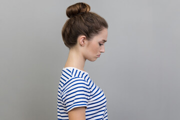 Side view of sad upset young adult woman wearing striped T-shirt expressing sadness, hearing bad...