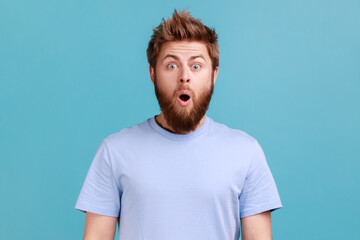 Portrait of shocked bearded man gasps from wonder, holds breath, stares at something horrible keeps...