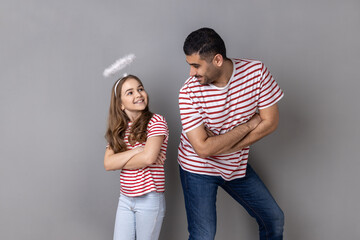Portrait of smiling joyful father and daughter in striped T-shirts standing with folded hands and...