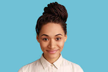 Portrait of pleasant woman with dreadlocks having perfect skin looking at camera with positive expression, beauty and care concept, wearing white shirt. Indoor studio shot isolated on blue background.