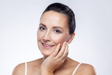 Closeup portrait of middle aged woman touching her face and looking at camera, enjoying the result of rejuvenation procedures, skin care concept. Indoor studio shot isolated on white background.