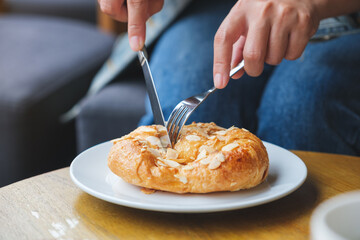 Closeup image of a woman holding and eating a fresh almond croissant with knife and fork