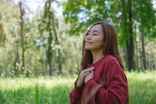 Portrait image of a young woman with closed eyes putting hands on her chest in the park