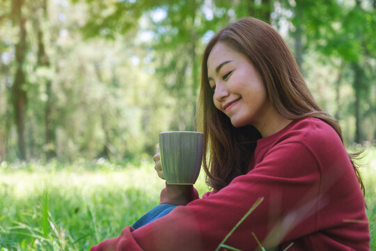 Portrait image of a beautiful young asian woman drinking coffee while sitting in the park