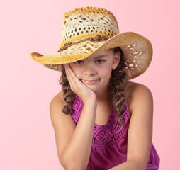 Biracial school age girl in cowboy hat isolated on pink background hand to chin - 521932850