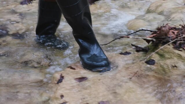 Man rubber boots river. Washes boots in cold water. Spring hike in the forest. High khaki fishing boots. The concept of rural life, hiking. travel, outdoor recreation. Walking on a mountain river