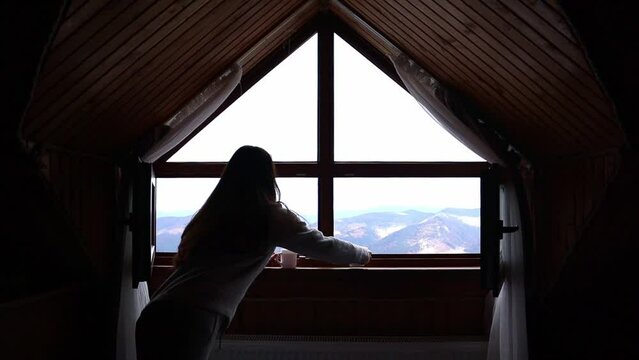 A young woman put on two cups of tea on the windowsill indoors in front of the beautiful mountains view