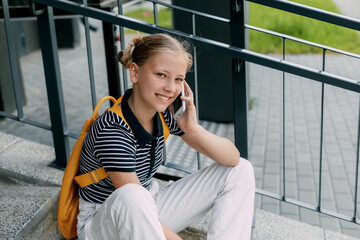 A beautiful girl is sitting on the stairs at school in between classes and talking on the phone