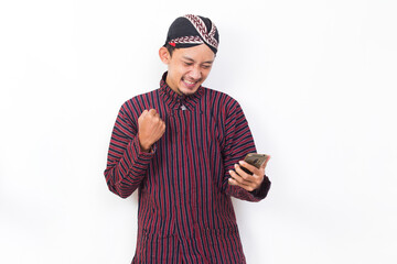 Happy joyful asian man with javanese traditional cloth lurik using mobile smartphone isolated on white background