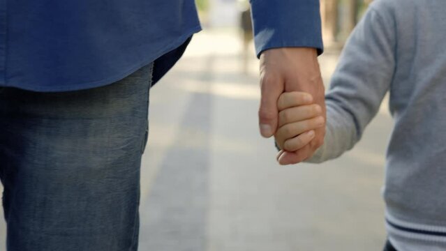 Close view of the father and sons hands. Father holds his son hands after school while going home. Father-son relationship and people concept