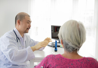 Fototapeta premium Asian confident doctor with stethoscope interacting with his senior patient in hospital