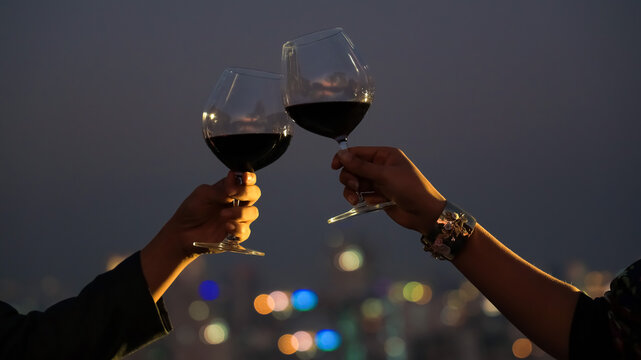 The Couple  hand with wine glasses have a romantic dinner on the rooftop with  sunset in a cityscape background