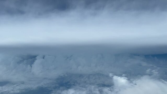 Unique aerial view from a jet cockpit flying near a huge and danderous cumulonimbus partially hidden by some stratus clouds at 12000 metres high. 4K.