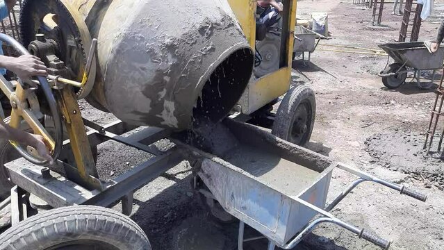 Concrete mixer pouring wet cement into the wheelbarrow. A close-up video of an diesel concrete mixer pouring wet cement into a wheelbarrow
