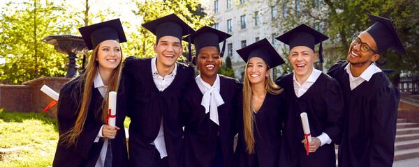 Happy diverse university graduates in green campus yard after graduation. Cheerful joyful students...