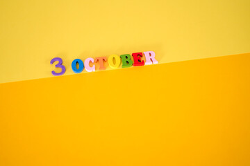 October 3 on a yellow, paper background with wooden and multicolored letters.