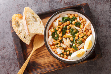 Chickpea stew with spinach and cod or potaje de vigilia close-up in a bowl on the wooden tray on the table. Horizontal top view from above