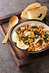 Potaje de Vigilia Spanish chickpea stew with cod and spinach close-up in a bowl on the wooden tray on the table. Vertical
