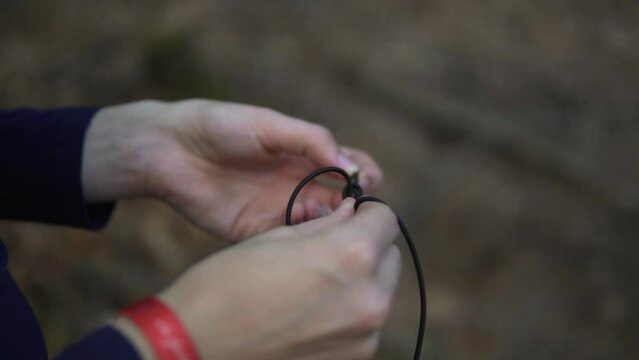 In a close-up video taken in a forest in Germany, a man is seen using his hands to tie a knot or knoten in a black rope.