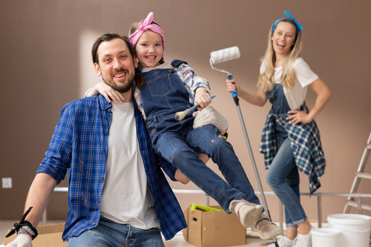 Portrait of happy smiling family repairing paint wall at home. Dad mom and child enjoy refreshing the color in the apartment. Working together and having fun.