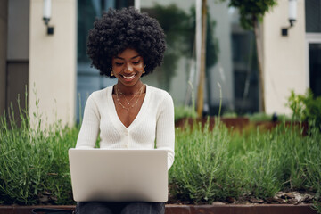 Young african american businesswoman working using laptop sitting on the bench in the city