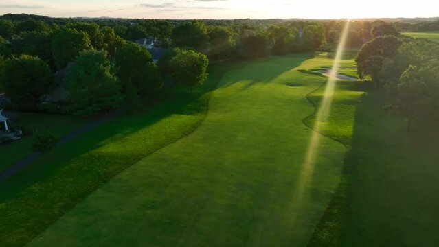 Aerial above golf course green fairway at sunset. Sand traps. Ball path tracking.