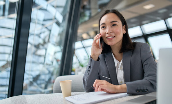 Young Busy Chinese Business Woman Talking On Phone Working In Modern Office. Asian Businesswoman Company Sales Client Manager Wearing Suit Making Call On Cellphone Sitting At Workplace.