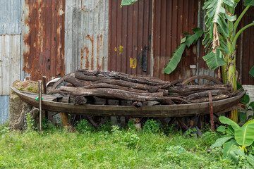 Old wooden boat in rustic rural setting with a stack of firewood and corrugated iron background
