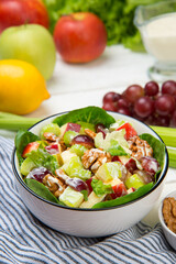 Waldorf salad of apples, celery stalks, walnuts, grapes, lettuce in a white salad bowl with ingredients on an old rustic white wooden table. Selected focus. - 521948421